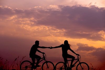 Die Silhouetten eines paares auf dem Fahrrad händchenhaltend vor dem Sonnenuntergang