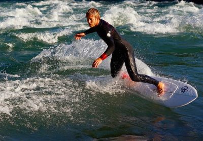 Ein Mann in Neoprenanzug surft auf einer Flusswelle