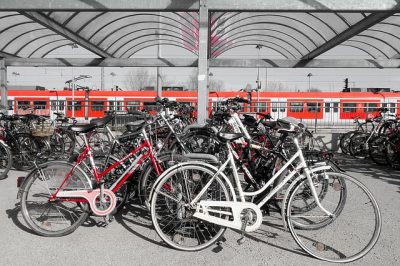 Überdachter Fahrradabstellplatz, dahinter fahrende S-Bahn, rot-weiß